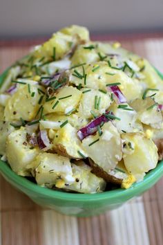 a green bowl filled with potato salad on top of a wooden table