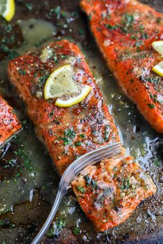 two salmon fillets with lemon slices and parsley on top, being served with a fork