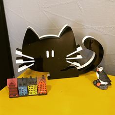 a black cat sitting on top of a table next to a toy penguin and house