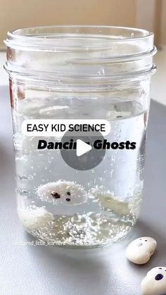 a glass jar filled with water next to two small white ghost heads on top of a table