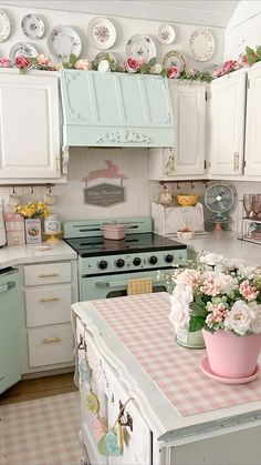 a kitchen filled with lots of white cabinets and pink flowers on top of a table