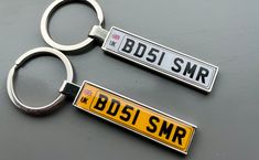 two metal key chains with the words bdsi srr and bsis smr on them