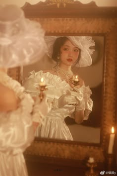 a woman wearing a white dress and holding a candle in front of a mirror with candles on it