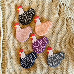 five chicken magnets sitting on top of a knitted blanket next to each other