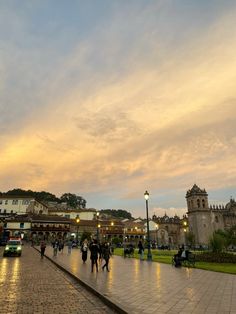 people are walking on the sidewalk in front of some buildings and trees at sunset or dawn