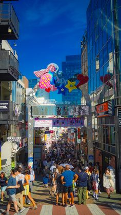 many people are walking down the street with kites in the air above them,