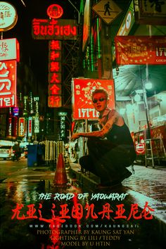 a woman sitting in the middle of a city at night with neon signs behind her