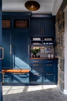 a kitchen with blue cupboards and stone walls, along with a wooden bench in the center