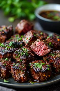 Grilled beef steak bites garnished with herbs on a plate, with a bowl of dipping sauce in the background. Air Fryer Steak Kebab Recipes, Air Fry Steak Bites Recipes, Air Fryer Teriyaki Steak Bites, Ribeye Steak Bites In Air Fryer, Healthy Air Fryer Steak Bites, Shell Steak Recipes, Steak Bits In Air Fryer, Air Fry Garlic Butter Steak Bites, Airfry Steak Bites Recipe