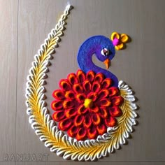 a peacock made out of yarn sitting on top of a wooden table next to a flower