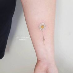 a small daisy tattoo on the left inner forearm and wristband, with a single flower attached to it