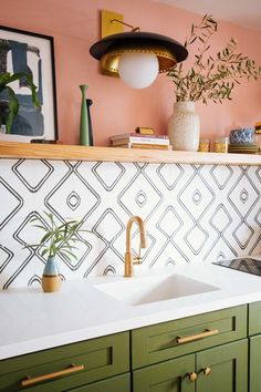 a kitchen with green cabinets and white counter tops, gold faucet, potted plant on shelf above sink