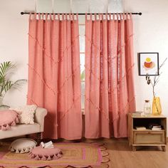 a living room with pink curtains and rugs in front of a window that is open