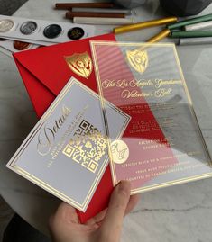 a person holding three red and silver cards with gold foil designs on them, next to some other items