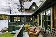 two chairs sitting on the front porch of a house with green siding and metal roofing