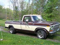 a brown and white truck parked on top of a grass covered field next to trees