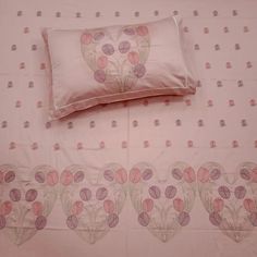 a bed with pink and purple flowers on it next to a white pillow cover that has hearts drawn on it