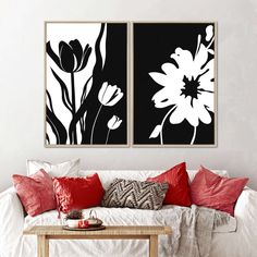 two black and white flowers are hanging on the wall above a couch with red pillows