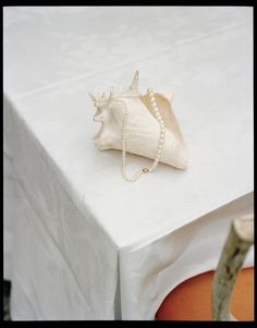 a white table cloth with a sea shell and pearls hanging from it's sides