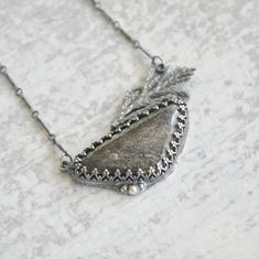 a silver necklace with a leaf design hanging from it's side on a marble surface