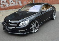 a black mercedes cls parked in front of a brick wall with graffiti on it