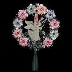 a flower arrangement with an angel in the center and flowers around it on a black background