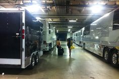 two large buses parked in a garage with people walking by them and luggage bags on the ground