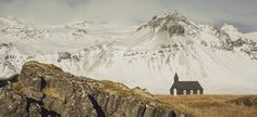 an old church on the side of a mountain with snow covered mountains in the background