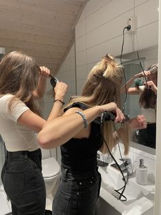 two women blow drying their hair in front of a mirror while another woman brushes her hair