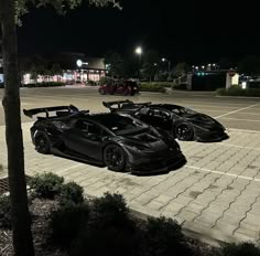 two black sports cars are parked in a parking lot at night with the lights on