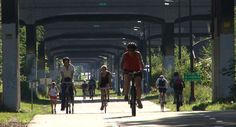 several people riding bikes down a street under an overpass