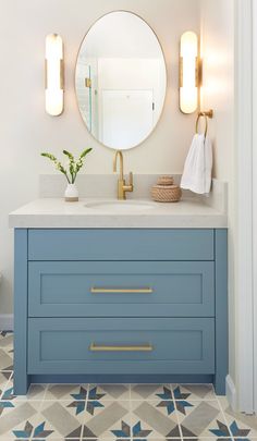 a bathroom vanity with blue drawers and gold handles on the countertop, along with a round mirror above it