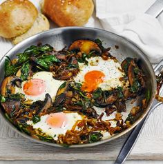 two fried eggs and spinach in a pan next to rolls on a white towel