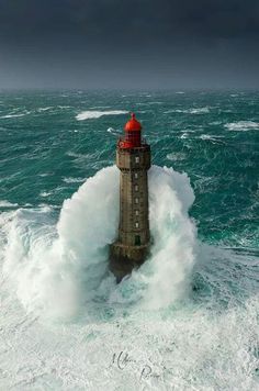 a lighthouse in the middle of an ocean with waves crashing around it and dark clouds overhead