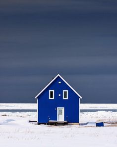 a blue house sitting in the middle of a snow covered field under a dark sky