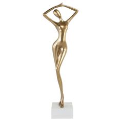 a gold statue is standing on a white surface with its hands behind her head and arms above her head