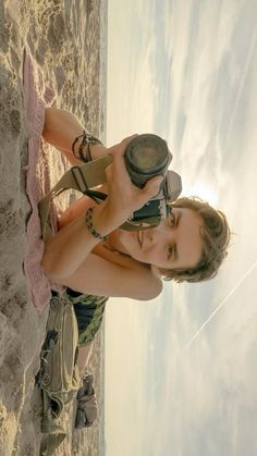 a woman standing on the beach holding a camera