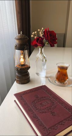 a red book sitting on top of a white table next to a vase with flowers