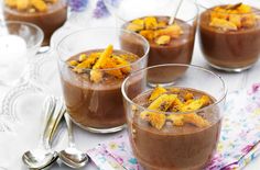 four glasses filled with dessert sitting on top of a white table covered in silverware