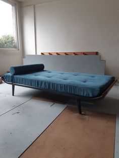 a blue bed sitting on top of a wooden floor next to a window in a room