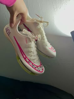 a child's hand holding onto a pair of white and pink shoes