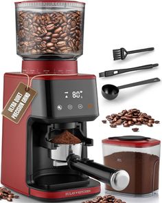 a red coffee maker sitting on top of a counter next to some coffee beans and spoons