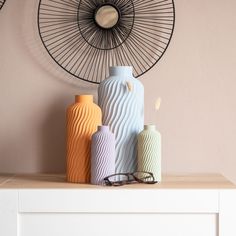 three vases sitting on top of a white dresser next to a wall clock and eyeglasses