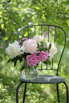 pink and white flowers are in a vase on a black chair with green foliage behind it