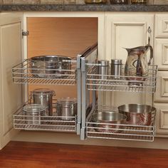 an open cabinet in a kitchen with pots and pans on the bottom shelf,