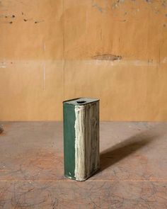 a green and white vase sitting on top of a floor next to a wall with peeling paint