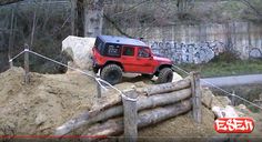 a red jeep parked on top of a pile of dirt next to a wooden fence