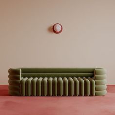 a green couch sitting on top of a pink floor next to a round wall clock