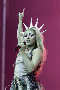 a woman dressed as the statue of liberty holding a microphone in one hand and wearing a crown on top of her head