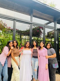 four women standing in front of a building with glass walls and plants on the outside